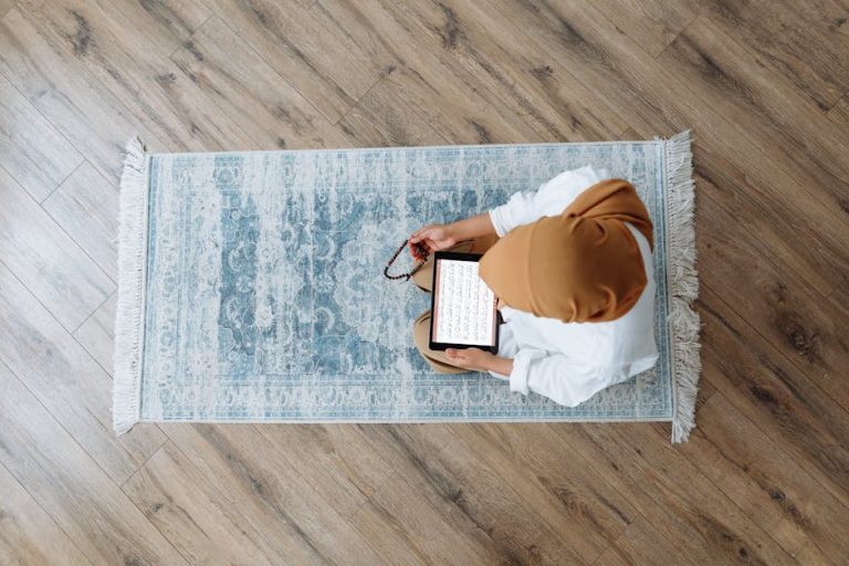 Overhead view of a Muslim woman praying with a tablet displaying scripture and holding prayer beads.