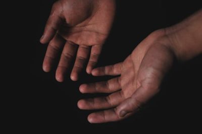 Close-up image of two hands with palms open against a black background, highlighting human skin texture.