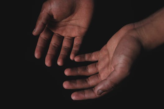 Close-up image of two hands with palms open against a black background, highlighting human skin texture.
