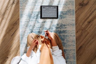 High-angle view of a person praying with prayer beads and Quran on a rug.