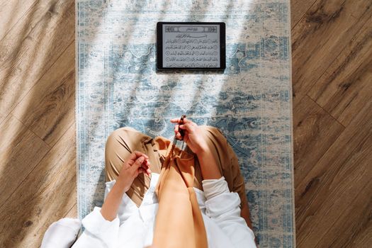 High-angle view of a person praying with prayer beads and Quran on a rug.