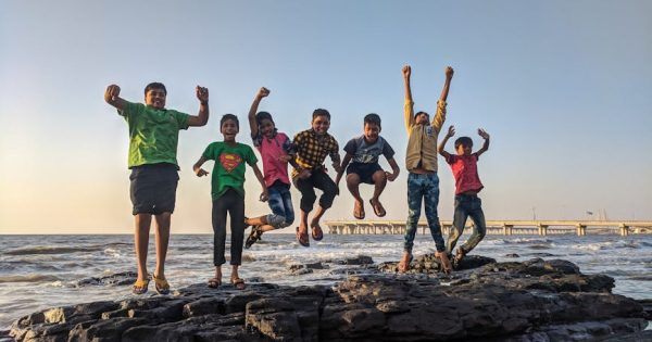 Group of kids joyfully jumping on rocks by the seaside. Fun and playful moment captured outdoors.